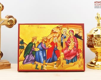 May include: A hand-painted icon depicting the Adoration of the Magi. Three kings, dressed in colorful robes, present gifts to the baby Jesus, who is seated on Mary's lap. The icon is set against a gold background with a red border.