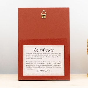 May include: A red rectangular icon with a certificate label, a gold-colored hanging bracket, and a gold-colored decorative object. The certificate text reads "Traditional Byzantine icon reproduction. High quality and excellent technique."