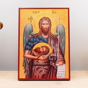 Puede incluir: Icono pintado a mano de San Juan Bautista sosteniendo la cabeza de San Juan Bautista. El icono está sobre un fondo de madera con un marco dorado. El icono está pintado en un estilo tradicional con colores vibrantes. El texto en el rollo dice "Metanoia to thetikos grin bi matou to ea non".