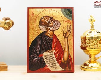 May include: A hand-painted icon of Saint John the Baptist, a religious figure in Christianity. The icon is painted on a wooden panel and features a gold background with a red and black robe. The icon is framed in a red wooden frame. The icon is a traditional Orthodox icon.