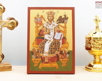 May include: A hand-painted icon of Jesus Christ, depicted as a king, sitting on a throne with a book in his hand. The icon is framed in a red wooden frame and has a gold background. The icon is part of a religious art collection.