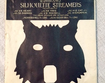 May include: A black and white silhouette of a wolf's head with a white background. The image is from a package of Dennison's Silhouette Streamers. The package lists the following designs: Heart, Shamrock, Tree, Red Bell, Cat, and Pumpkin. The package also lists the length of the streamers and the bells.