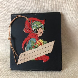 May include: A vintage black gift tag with a colorful illustration of a girl wearing a red hooded cloak and holding a gift box. The tag has a string attached and a blank space for writing "For" and "From".