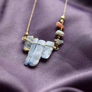 May include: A gold chain necklace with a pendant made of several blue kyanite stones. The stones are arranged in a staggered pattern and are held together by a thin gold wire.