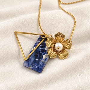 May include: A gold chain necklace featuring three charms: a polished gold triangle, a rectangular blue and white sodalite stone pendant, and a textured gold flower charm with a central white pearl accent.
