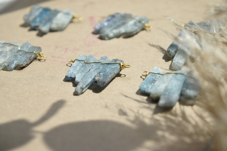 May include: Five sets of blue kyanite crystal clusters, each wired with gold jump rings, arranged on a light brown surface.