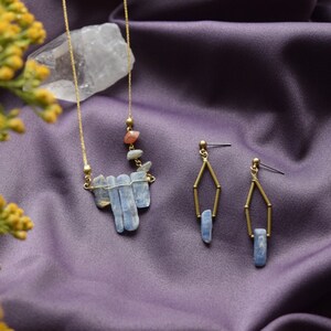 May include: A gold necklace with a pendant made of blue and clear crystal stones. Two matching earrings with blue crystal stones hang from gold hoops.