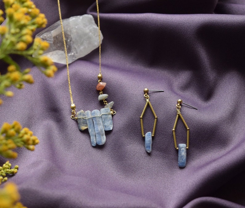 May include: A gold necklace with a pendant made of blue and clear crystal stones. Two matching earrings with blue crystal stones hang from gold hoops.
