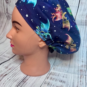 May include: A blue scrub hat with a repeating pattern of dragons and stars. The dragons are green, gold, and pink.