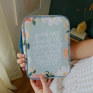 May include: A blue floral bible cover with the quote "perhaps this is the moment for which you were created" and the scripture reference "Esther 4:14".