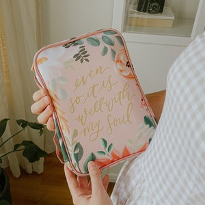 May include: A pink floral zippered pouch with a gold inscription that reads "even so it is well with my soul".