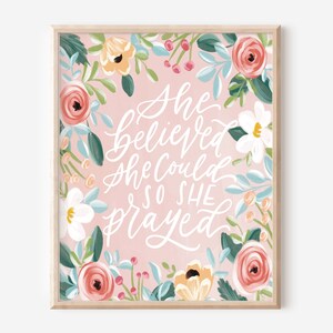 May include: A pink floral print with a white handwritten quote that reads "She believed she could so she prayed".