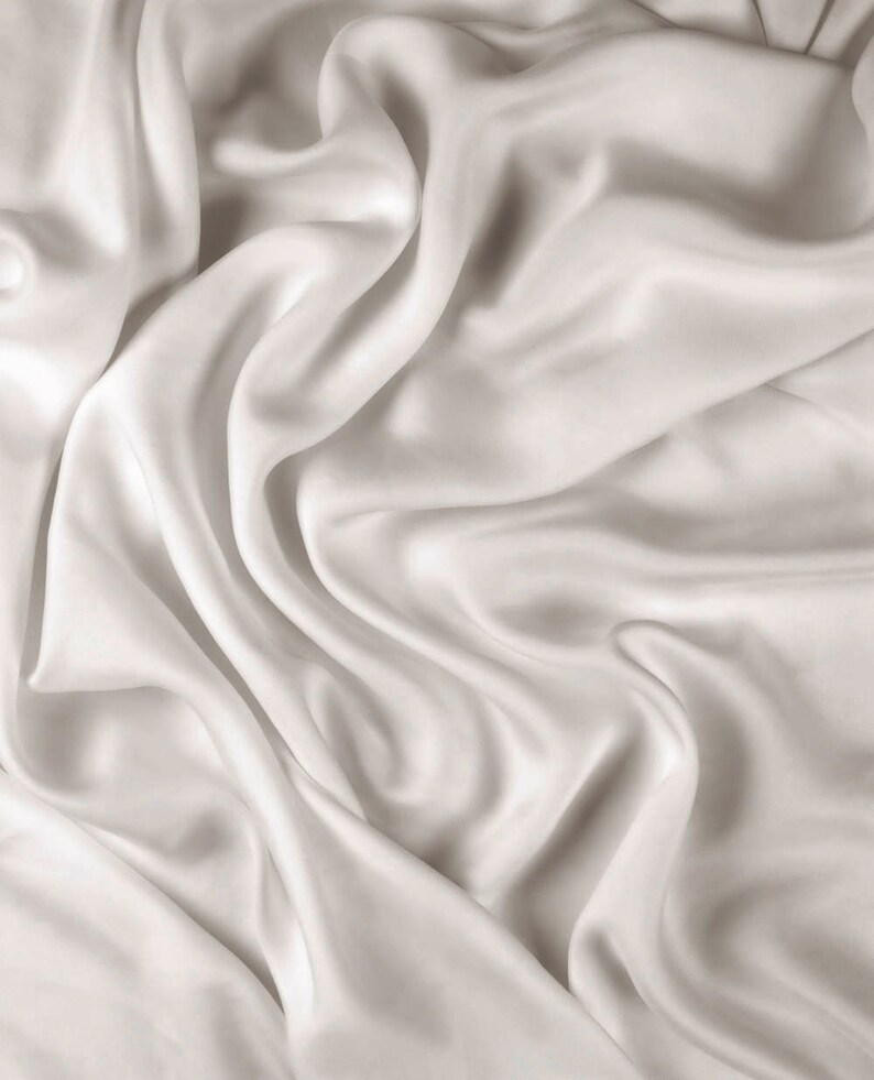 May include: A close-up of smooth, white satin fabric with soft, flowing folds and wrinkles.