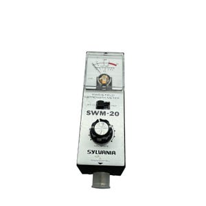 Puede incluir: Un medidor de SWR y de intensidad de campo Sylvania SWM-20 con carcasa negra rectangular y placa frontal plateada. El dispositivo incluye un medidor de aguja analógico, un interruptor negro FWD/REF, un mando de calibración y un conector.