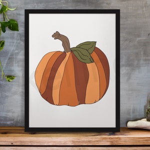 May include: A framed print of a stylised illustration of a pumpkin with brown and orange stripes and green leaves.