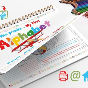 Puede incluir: Un cuaderno de trabajo del alfabeto con espiral, con el título "Mon premier - My First Alphabet" en inglés y francés. La portada presenta una ilustración de un biplano rojo. Se ven lápices de colores en el fondo.