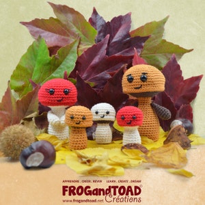 Puede incluir: Un grupo de figuras de setas de ganchillo con caras sonrientes, en varios colores como rojo, marrón y blanco, dispuestas con hojas de otoño y castañas. La imagen incluye el texto "FROG and TOAD Créations".
