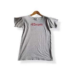 Könnte beinhalten: Ein graues T-Shirt mit einem roten 45rpm-Aufdruck auf der Vorderseite.