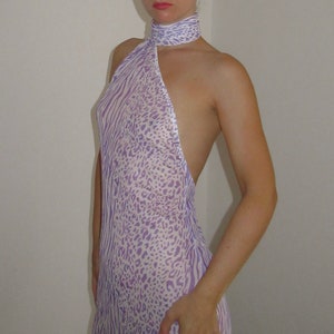 May include: A woman wearing a purple and white animal print halter top with a sheer fabric. The top has a high neckline and a halter strap.