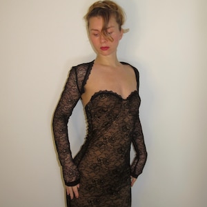 May include: A black lace dress with long sleeves and a sweetheart neckline. The dress is form-fitting and appears to be made of delicate, see-through lace. The sleeves are attached to a bolero-style top.