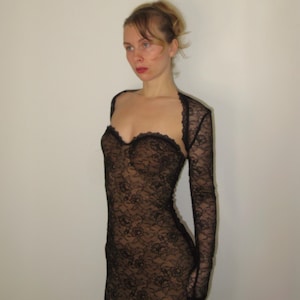 May include: A black lace dress with long sleeves. The dress features a sweetheart neckline and a fitted silhouette. The lace pattern is intricate and detailed, creating a delicate and elegant look. The dress is a formal wear item.