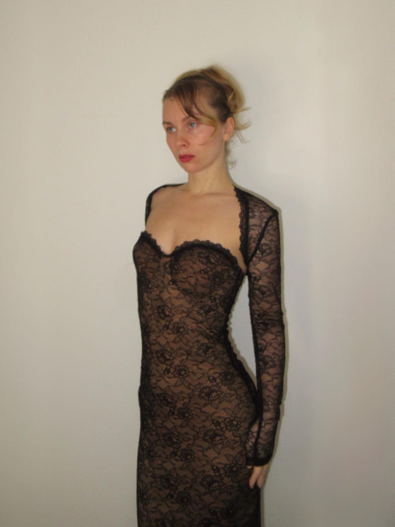 May include: A black lace dress with long sleeves. The dress features a sweetheart neckline and a fitted silhouette. The lace pattern is intricate and detailed, creating a delicate and elegant look. The dress is a formal wear item.