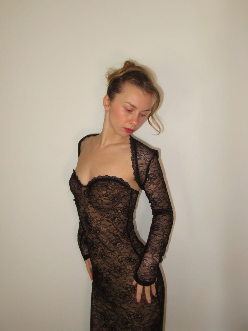 May include: Black lace dress with a sweetheart neckline and long sleeves. The dress is form-fitting and made of a delicate, see-through lace fabric. The sleeves are attached to a bolero-style top.