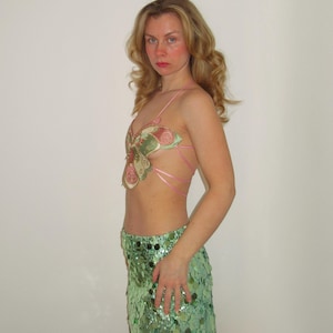 May include: A woman wearing a green sequined skirt and a pink and green butterfly-shaped top.