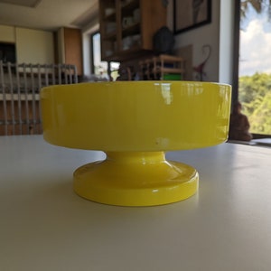 May include: A bright yellow ceramic pedestal bowl with a wide, round base. The bowl is smooth and glossy.