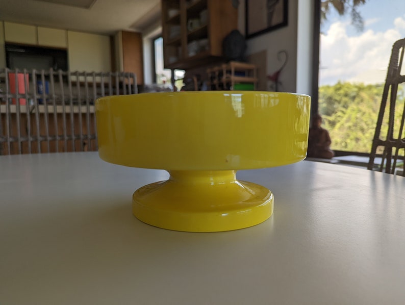 May include: A bright yellow ceramic pedestal bowl with a wide, round base. The bowl is smooth and glossy.