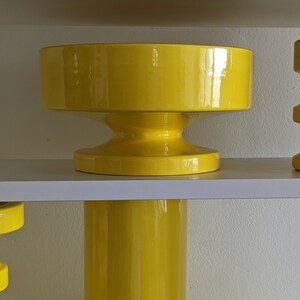 May include: A set of three yellow ceramic planters with a modern design. The planters are stacked on a white shelf.