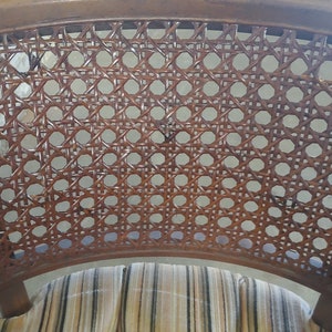 May include: A close-up of the woven cane back of a chair. The cane is brown and has a woven pattern. The chair has a striped fabric seat.