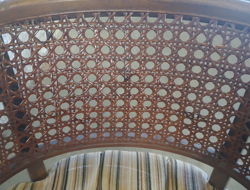May include: A close-up of the woven cane back of a chair. The cane is brown and has a woven pattern. The chair has a striped fabric seat.