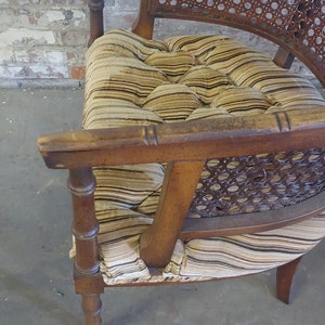 May include: A wooden chair with a woven cane back and seat. The chair has a brown and beige striped fabric cushion with tufted buttons.