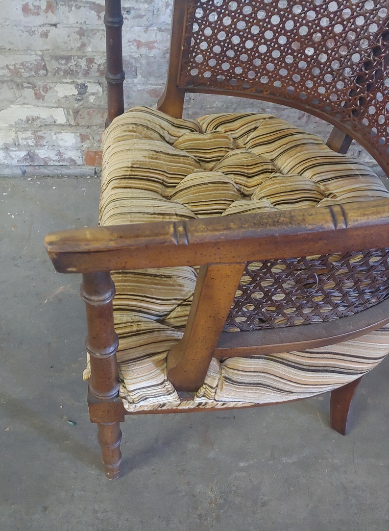 May include: A wooden chair with a woven cane back and seat. The chair has a brown and beige striped fabric cushion with tufted buttons.