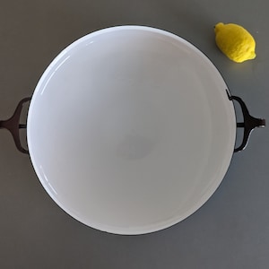 May include: White enamelware baking dish with black handles. The dish is empty and has a slight curve to the bottom.