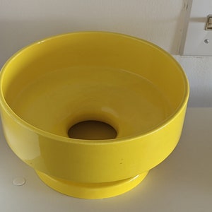 May include: A bright yellow ceramic planter with a wide, round opening and a smaller, round base. The planter is made of a smooth, glossy ceramic.