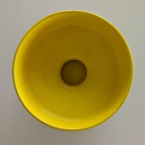 May include: A bright yellow ceramic bowl with a round opening in the center. The bowl is empty.