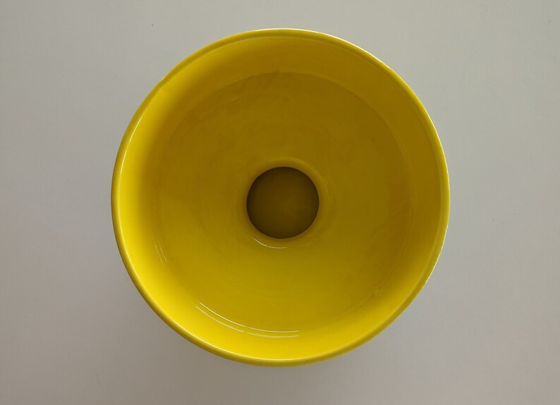 May include: A bright yellow ceramic bowl with a round opening in the center. The bowl is empty.