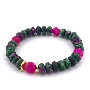 May include: A bracelet made of green and magenta gemstones. The bracelet features a mix of round and faceted beads, with gold-coloured spacers. The gemstones are arranged in a circular pattern, creating a vibrant and eye-catching accessory.