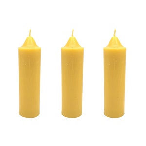 May include: Three yellow beeswax candles, each with a pointed top and a smooth, cylindrical shape.