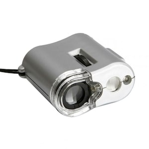 Puede incluir: Un microscopio de mano plateado con una lente transparente y una luz LED integrada. El microscopio tiene un botón de ajuste de enfoque y un cable de alimentación.