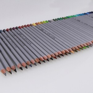 May include: A set of 48 colored pencils with a silver barrel and a wood casing. The pencils are arranged in a row, with the tips facing the viewer. The pencils are labeled with the brand name "RAINBOW COLOR" and a number.