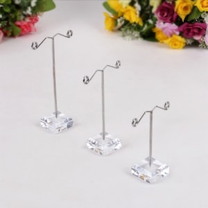 Peut inclure: Trois présentoirs à boucles d'oreilles en acrylique transparent avec des supports à boucles d'oreilles en métal argenté. Chaque présentoir a une base carrée et un seul poteau vertical avec un fil incurvé en haut pour tenir les boucles d'oreilles.