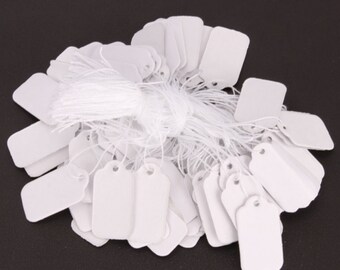 May include: A pile of white rectangular hang tags with string attached. The tags are blank and ready for writing.