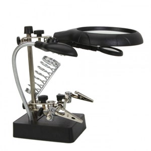 May include: A black magnifying glass with a light and two adjustable clamps on a black base. The magnifying glass has a flexible gooseneck arm and a spring-loaded holder.