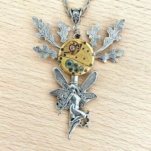 May include: A silver key necklace with a fairy figure and wings, a clockwork face, and silver leaves. The necklace is on a gold chain.