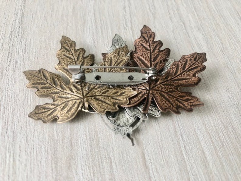 Peut inclure: Une broche en forme de trois feuilles d'&eacute;rable, tonifi&eacute;e or, argent et cuivre.