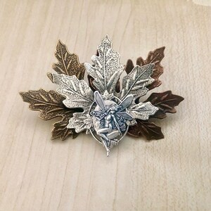 Peut inclure: Une figurine de f&eacute;e argent&eacute;e avec des ailes est plac&eacute;e au centre d'un groupe de trois feuilles argent&eacute;es et bronze. Les feuilles sont textur&eacute;es et pr&eacute;sentent un design d&eacute;taill&eacute;.