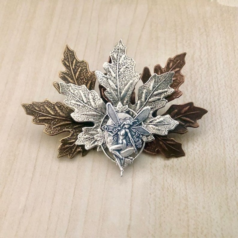 Peut inclure: Une figurine de f&eacute;e argent&eacute;e avec des ailes est plac&eacute;e au centre d'un groupe de trois feuilles argent&eacute;es et bronze. Les feuilles sont textur&eacute;es et pr&eacute;sentent un design d&eacute;taill&eacute;.